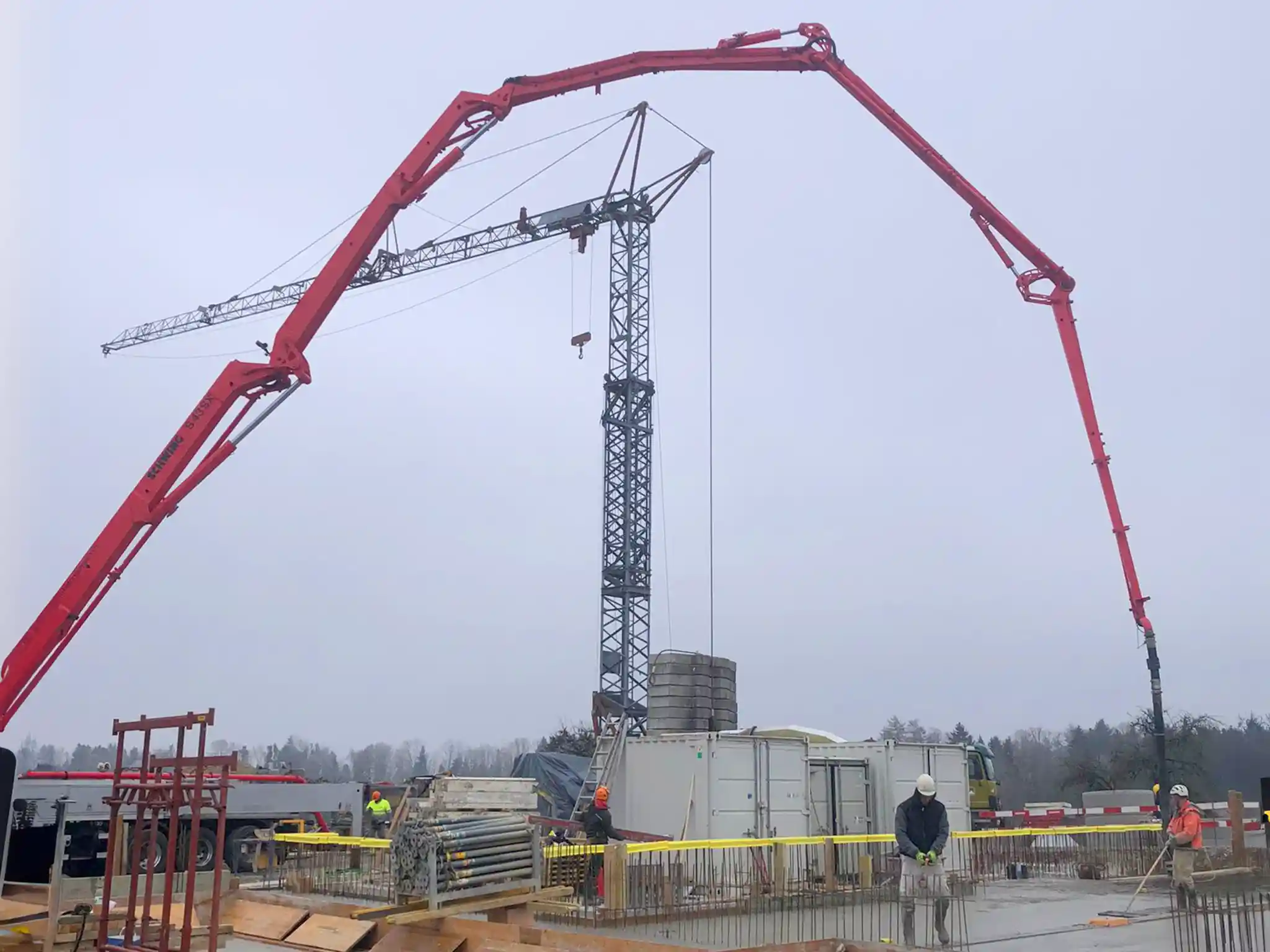 Baustelle während der Betonierarbeiten mit Betonpumpe, Turmdrehkran und Arbeitern im Fundamentbereich