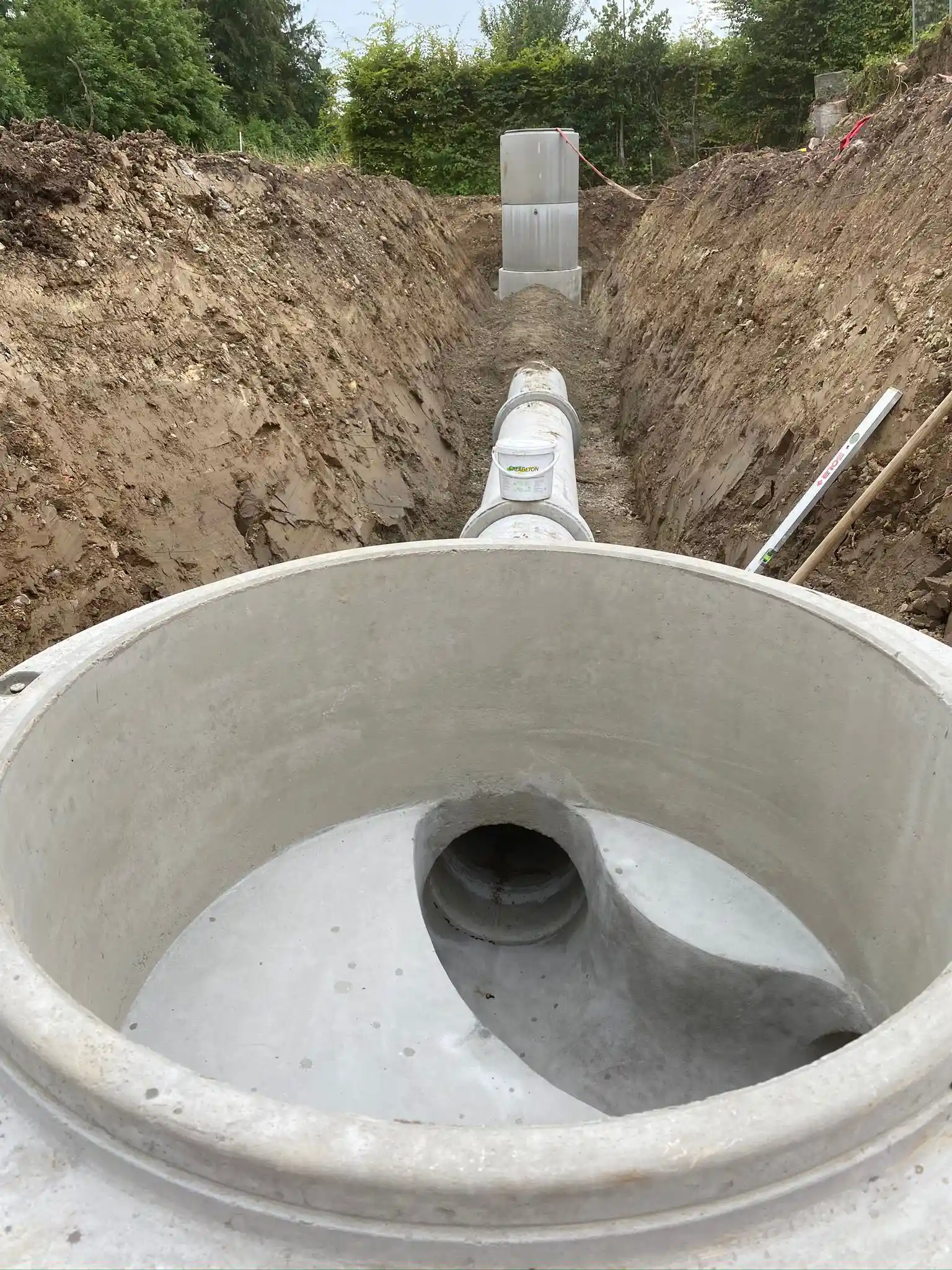 Blick in einen Entwässerungsschacht auf einer Baustelle mit verlegten Betonrohren in einem langen, offenen Graben.